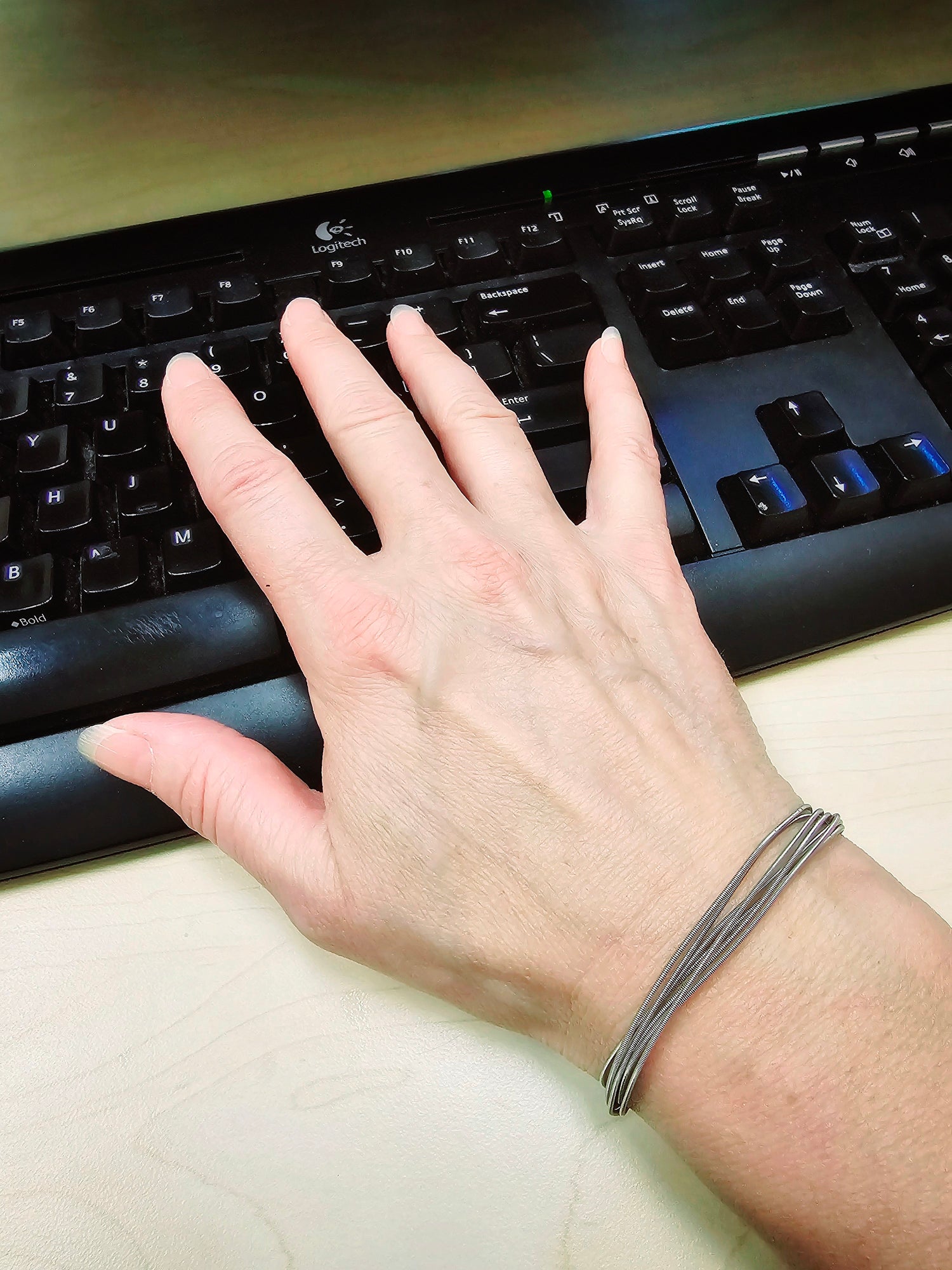 Hand sitting on a black keyboard on wrist is a multi-strand upcycled guitar string bracelet