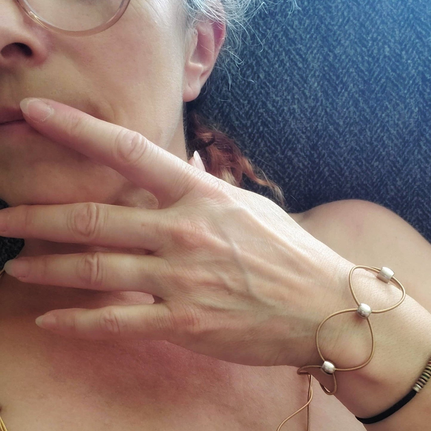 Hand and face of woman wearing a gold and silver coloured guitar string bracelet
