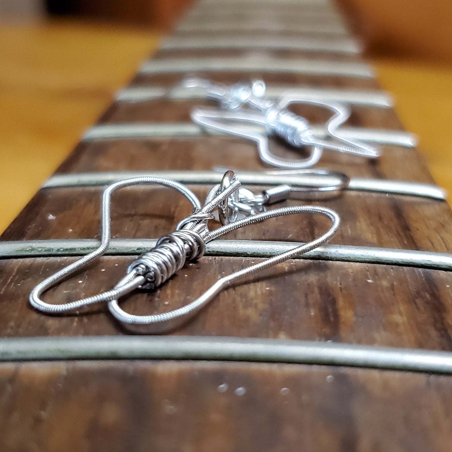 a pair of earrings, the first one is clear the second one further back is blurred - both are made from upcycled guitar strings shaped into butterflies  - earrings are sitting on the neck of a guitar which has no strings