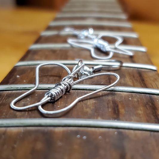 a pair of earrings, the first one is clear the second one further back is blurred - both are made from upcycled guitar strings shaped into butterflies  - earrings are sitting on the neck of a guitar which has no strings