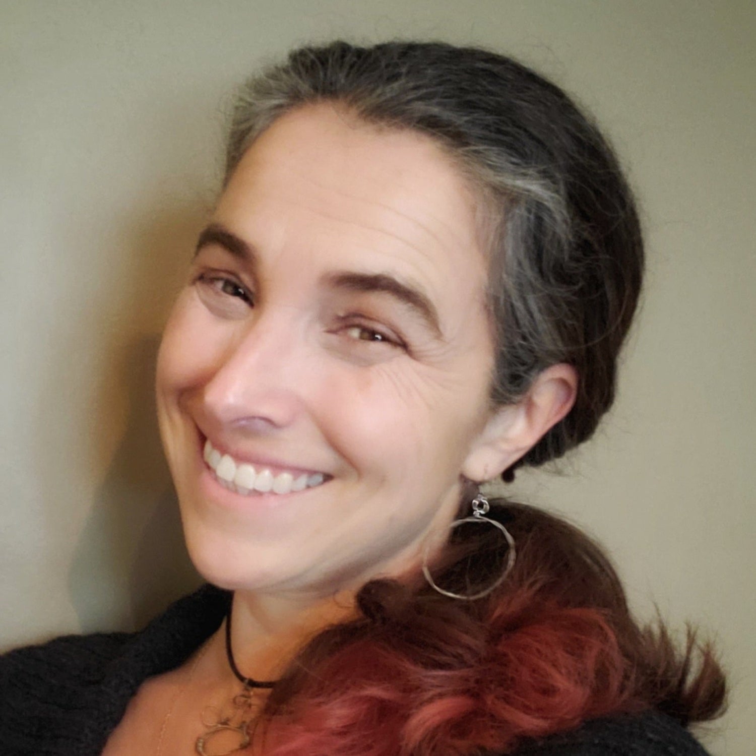 left side of a smiling woman's head with brown, grey and red hair she is wearing a hoop style silver coloured earring made from an upcycled guitar string - she is also wearing a necklace with a dog paw pendant made from an upcycled guitar string and a black leather cord