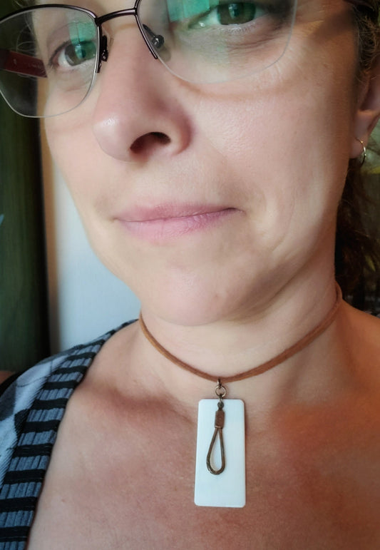 face of a woman with glasses wearing a necklace made from an upcycled ivory piano key topper and a teardrop shaped upcycled piano string both hanging on a brown suede chord