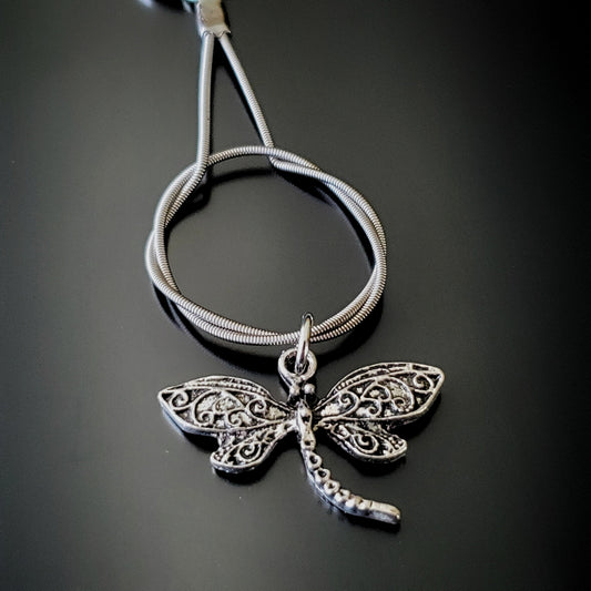closeup of a silver coloured keychain made from an upcycled guitar string on which hangs a silver coloured dragonfly pendant