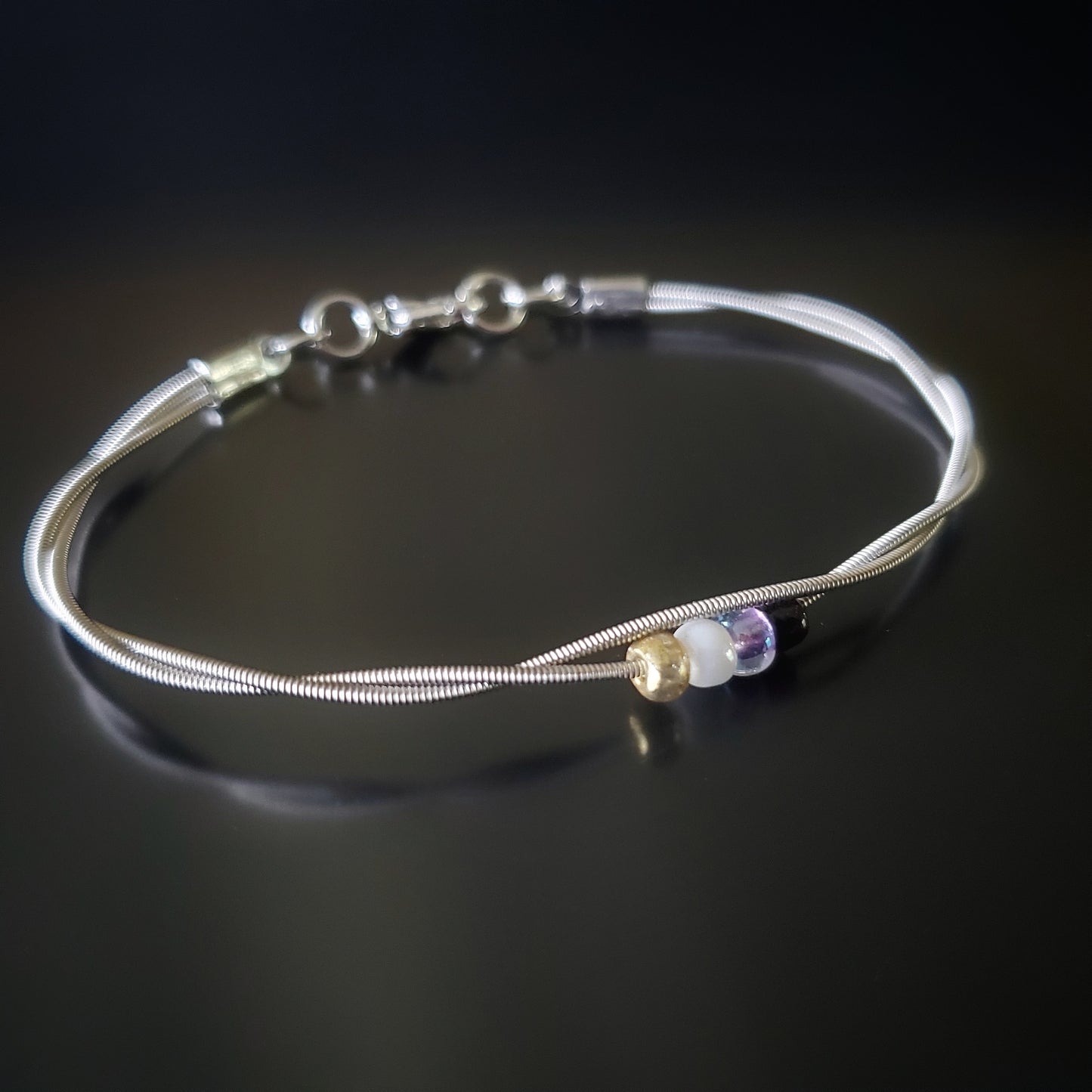 silver coloures clasp style bracelet with 4 glass beads representing the non-binary flag (yellow, white, purple & black)