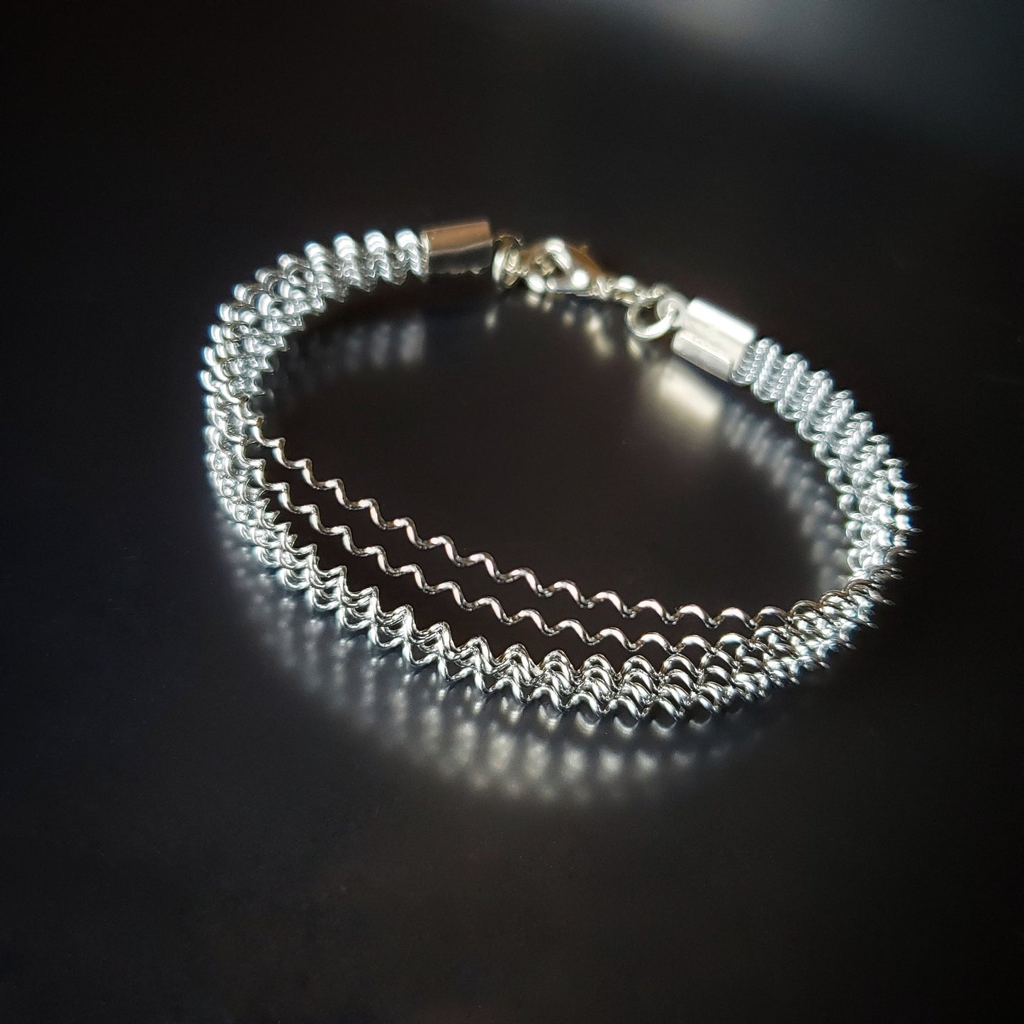 silver coloured clasp style bracelet made from a series of upcycled snare drum strings