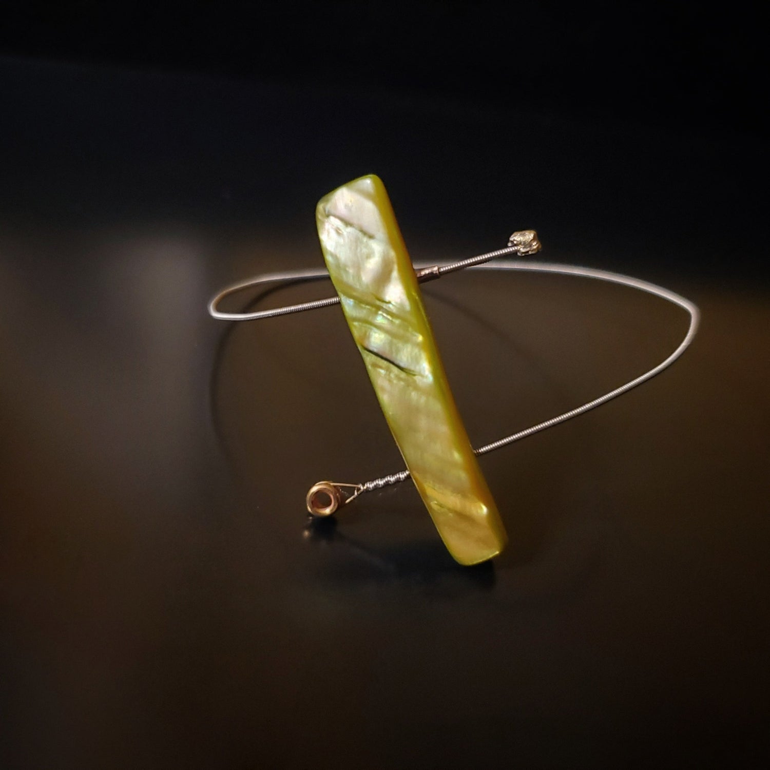 spiral style bangle bracelet made from an upcycled guitar string and a piece of shell in the shape of a rectagle