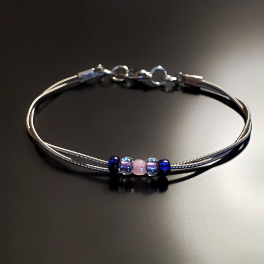 guitar string bracelet with blue, purple and pink bead representing the bisexual pride flag -black background