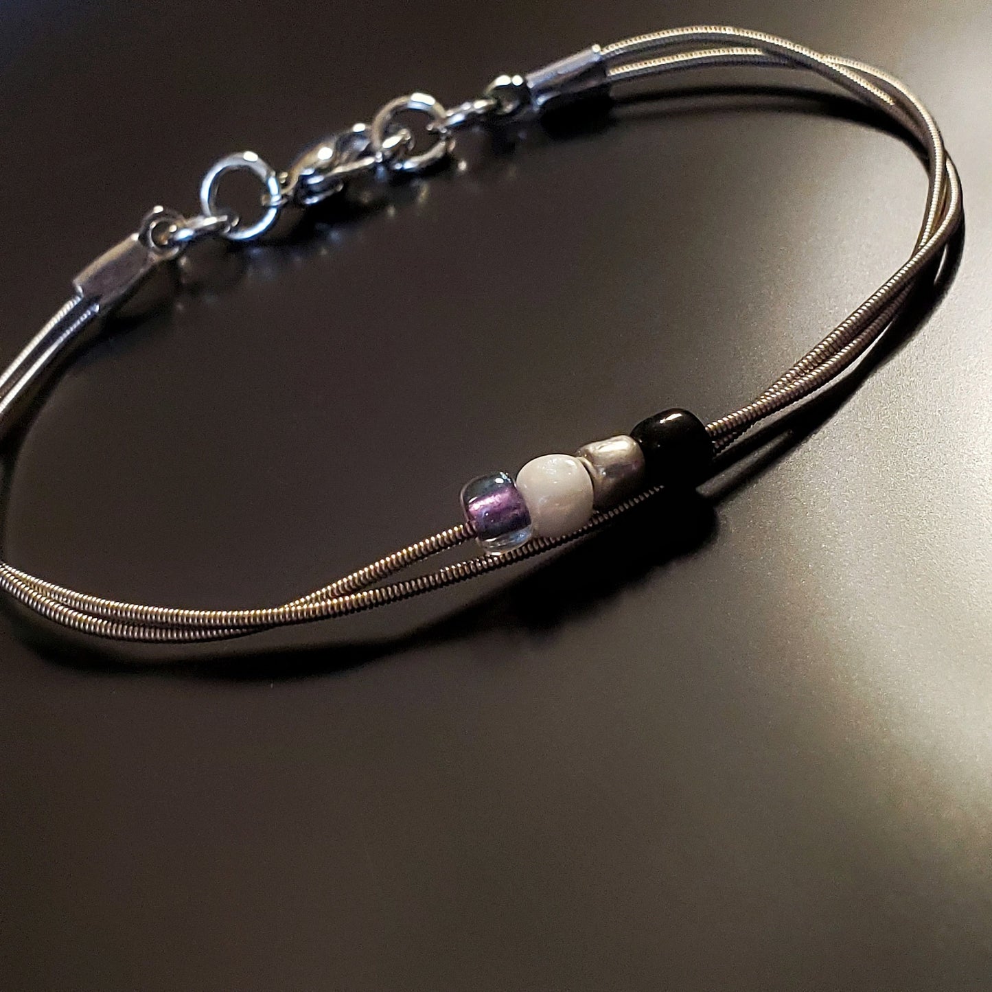 silver coloures clasp style bracelet with 4 glass beads representing the asexual pride flag (black, grey, white & purple)