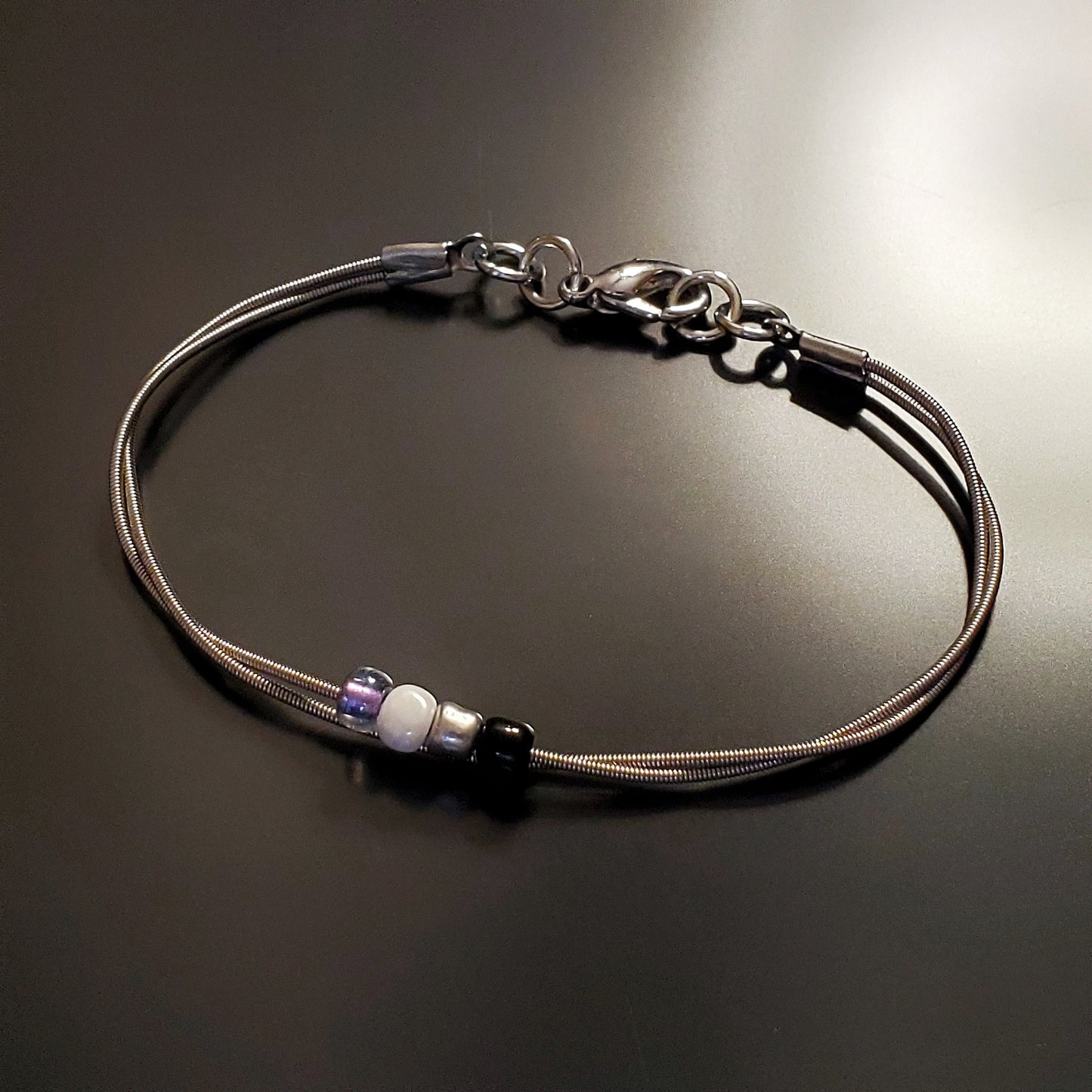 silver coloures clasp style bracelet with 4 glass beads representing the asexual pride flag (black, grey, white & purple)