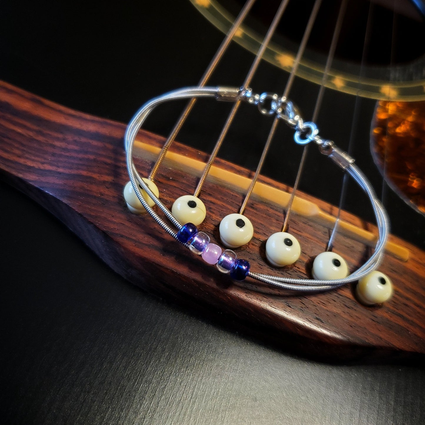 guitar string bracelet with blue, purple and pink bead representing the bisexual pride flag lying on a black guitar