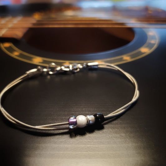 silver coloures clasp style bracelet with 4 glass beads representing the asexual pride flag (black, grey, white & purple)