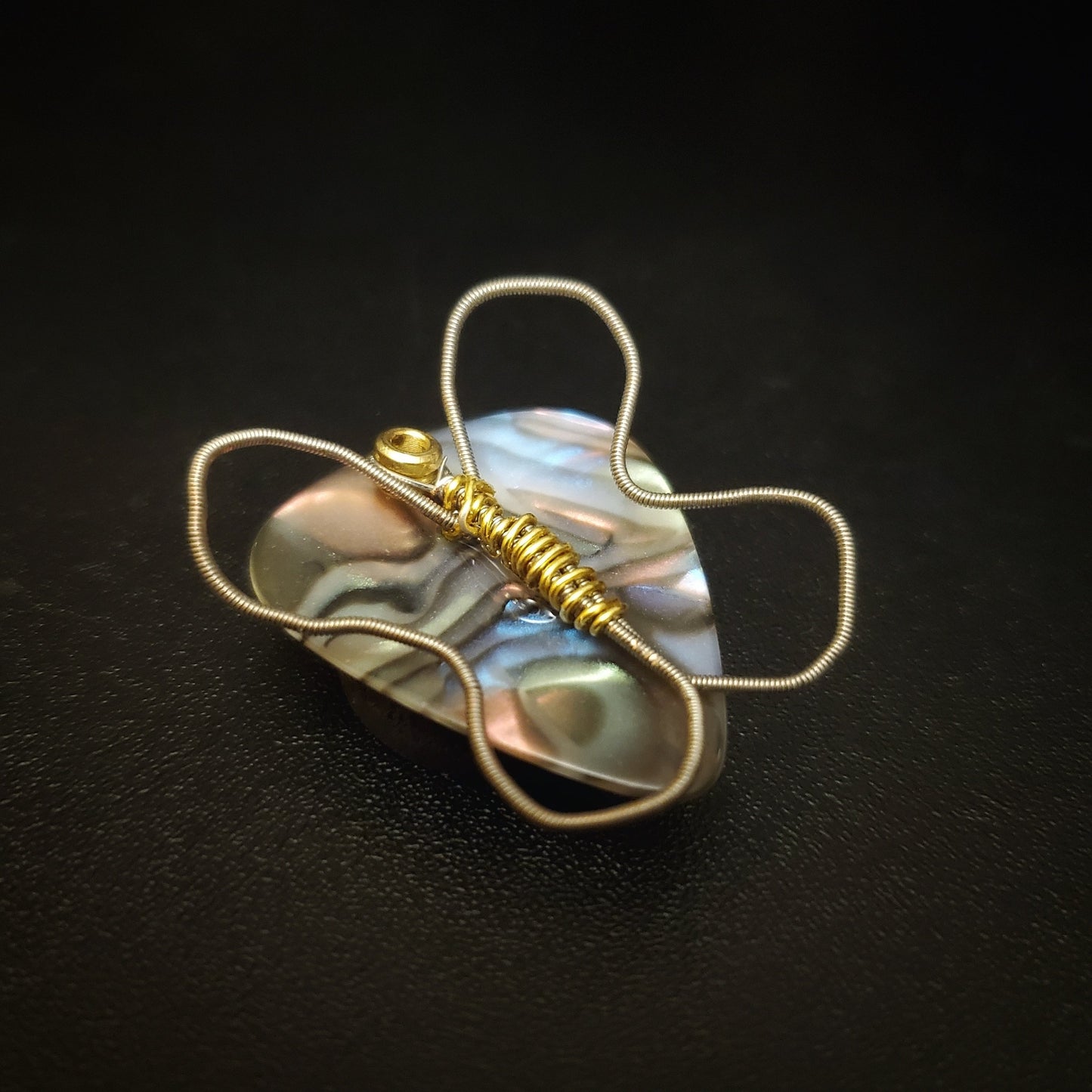 a magnet made from an upcycled guitar string shaped like a butterfly sitting on a multicoloured guitar pick - black background