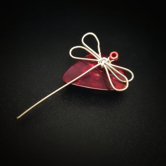 magnet made from an upcycled guitar string shaped like a dragonfly sitting on a dark red guitar pick - black background