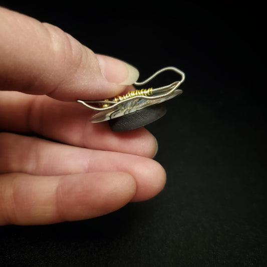 fingers holding a magnet made from an upcycled guitar string shaped like a butterfly sitting on a multicoloured guitar pick - black background