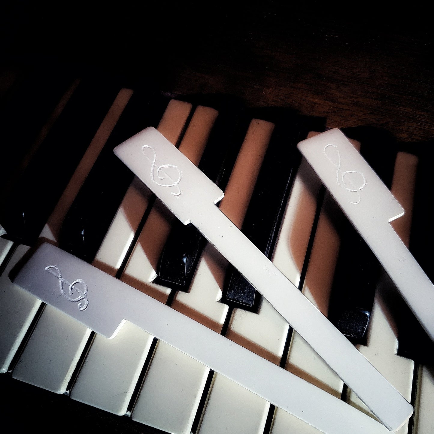 Three bookmarks made from white piano key toppers-a treble clef has been etched on each one -they are lying on piano keys