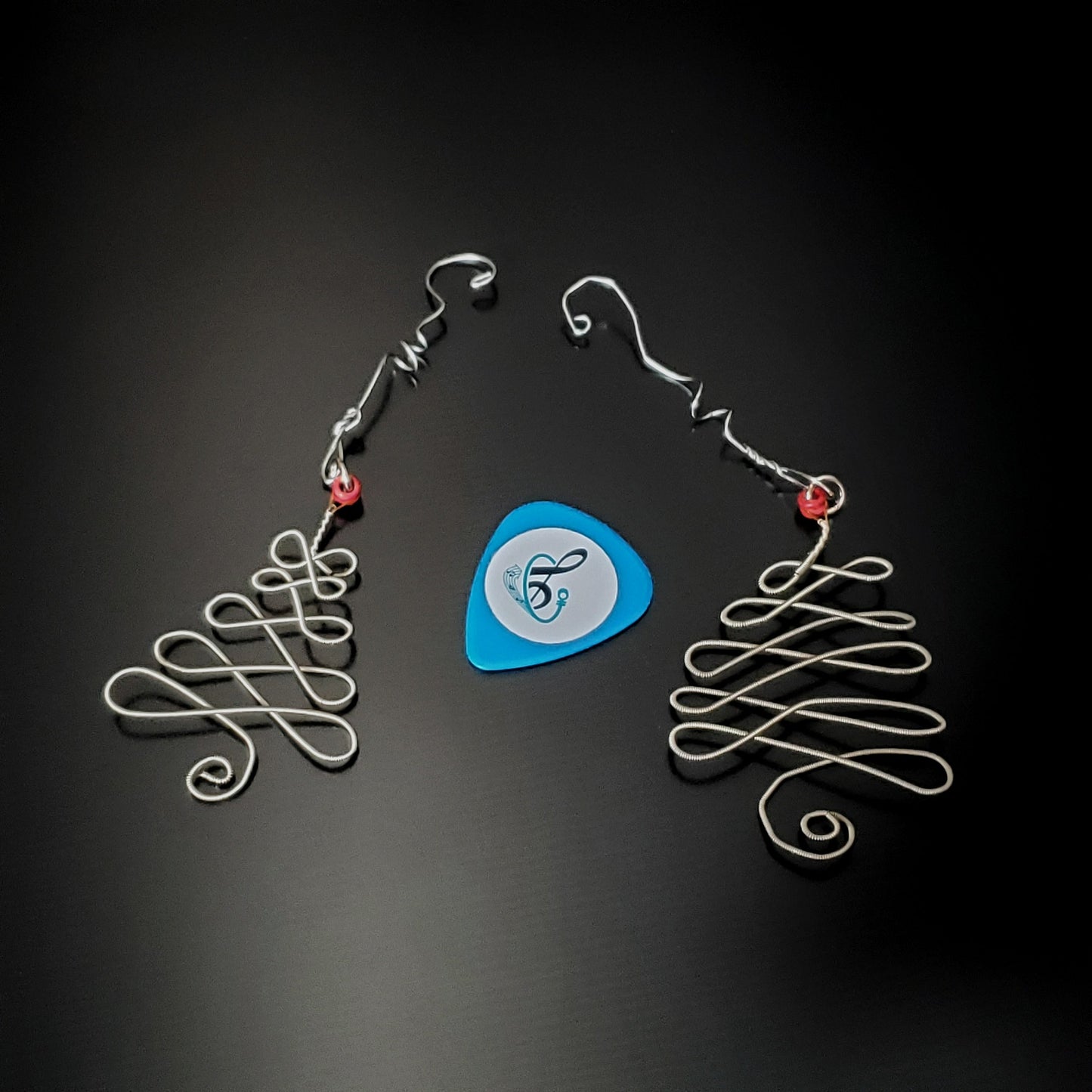 2 silver coloured christmas decorations in the shape of a christmas tree made from an upcycled guitar string next to a light blue guitar pick