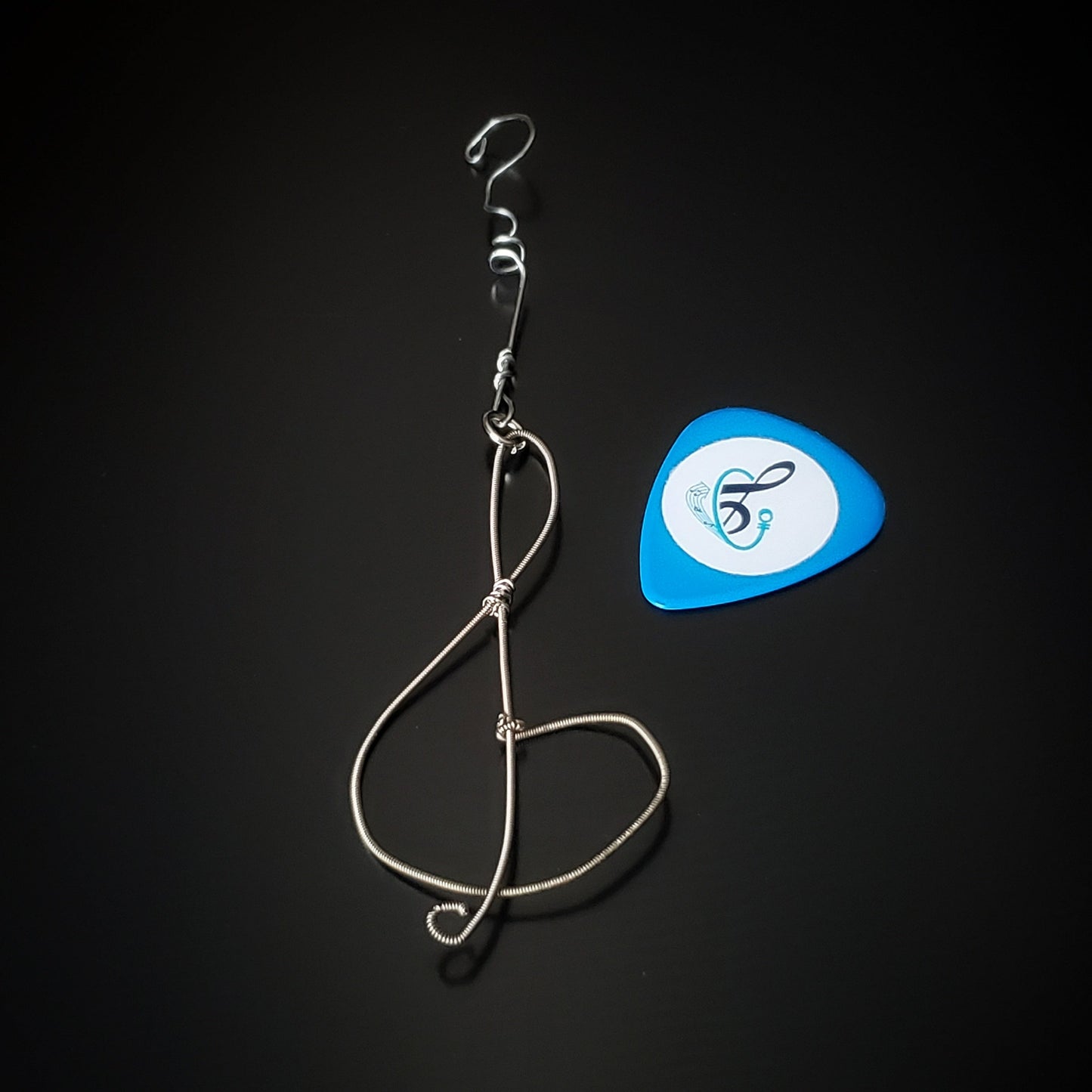 Christmas ornament in the shape of a treble clef, made from an upcycled guitar string - on the left is a blue guitar pick