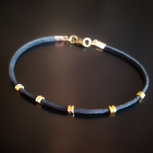bracelet made from black suede cord and gold coloured guitar string ballends on a black background