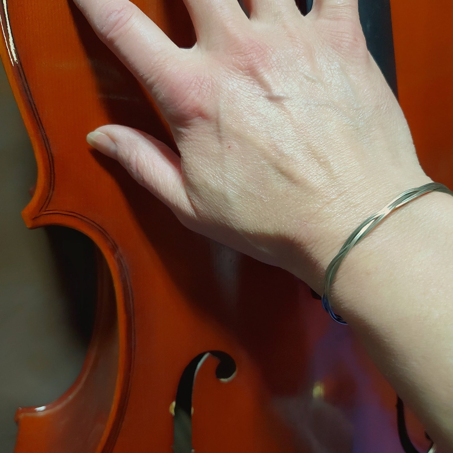 hand wearing an upcycled cello string unisex silver bracelet -touching a cello