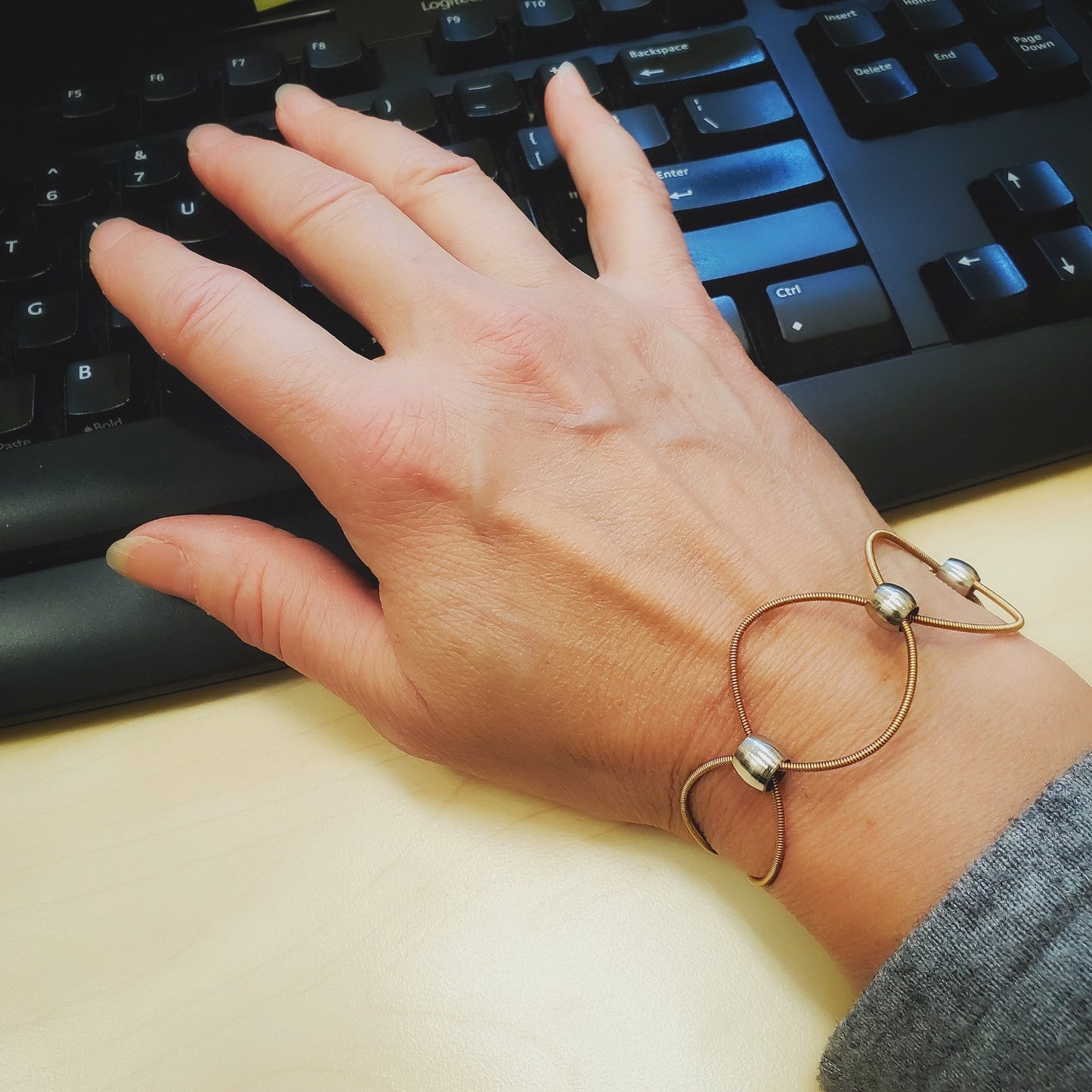 hand resting on a keyboard - on wrist is a upcycled guitar strings bracelet with silver coloured beads