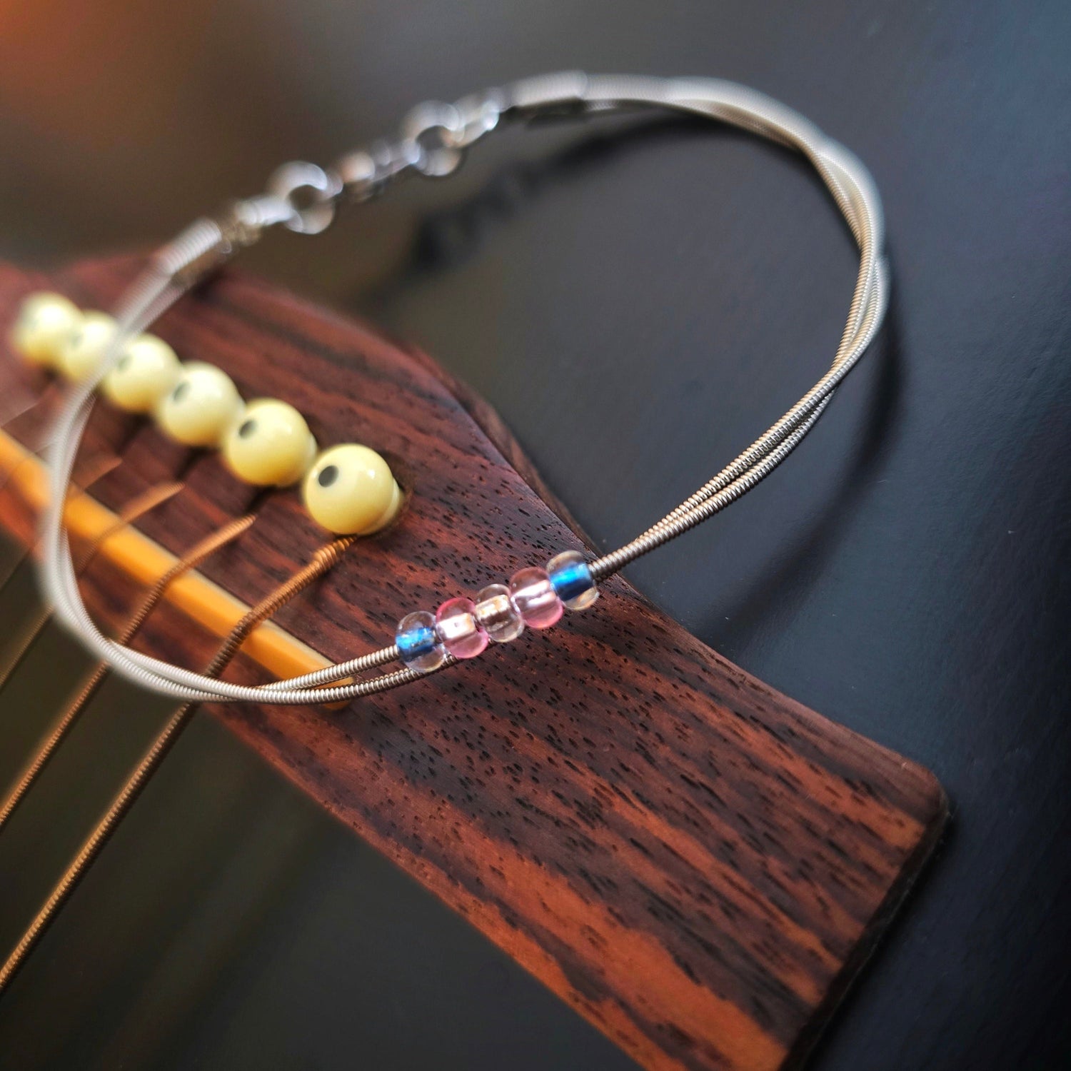 Guitar string trans pride bracelet on black guitar