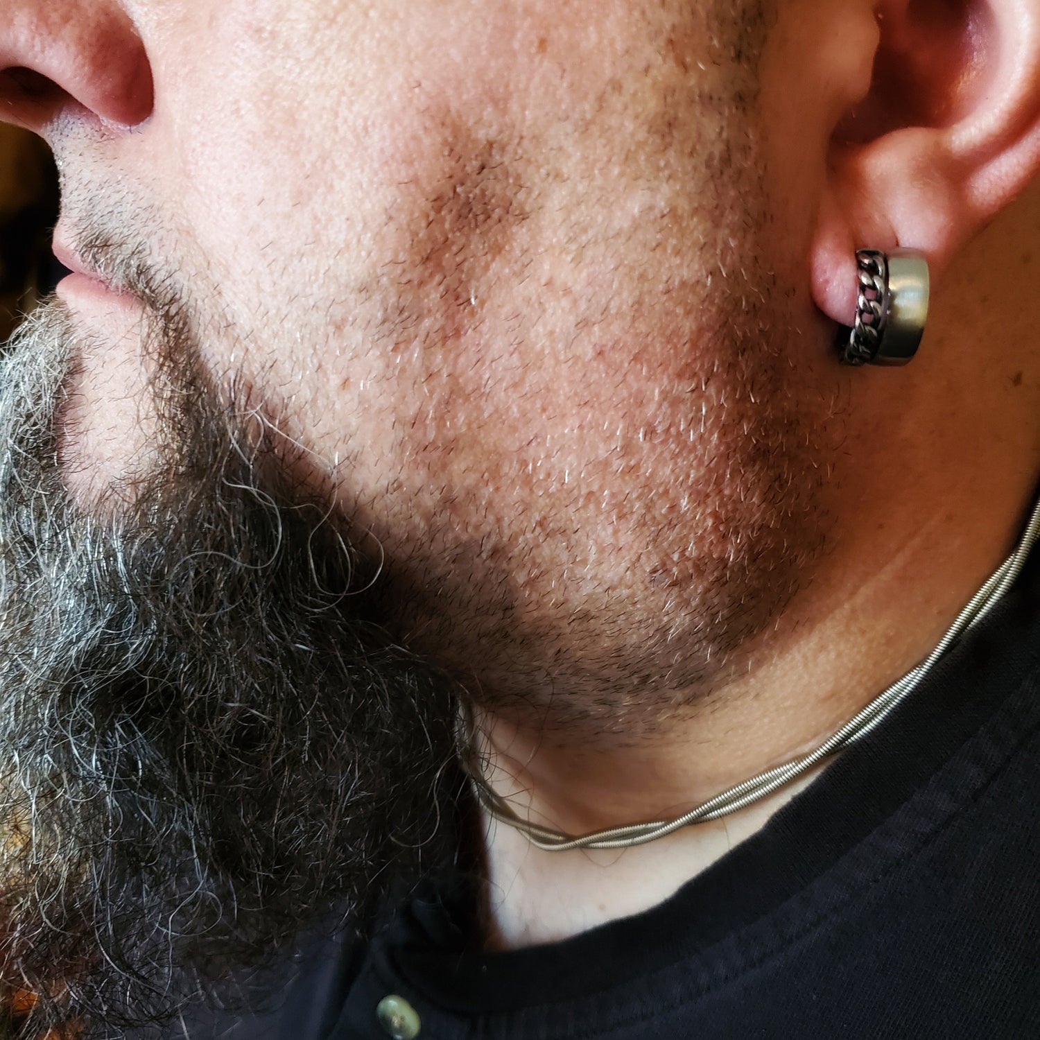 man's profile, wearing silver coloured electric bass guitar string necklace