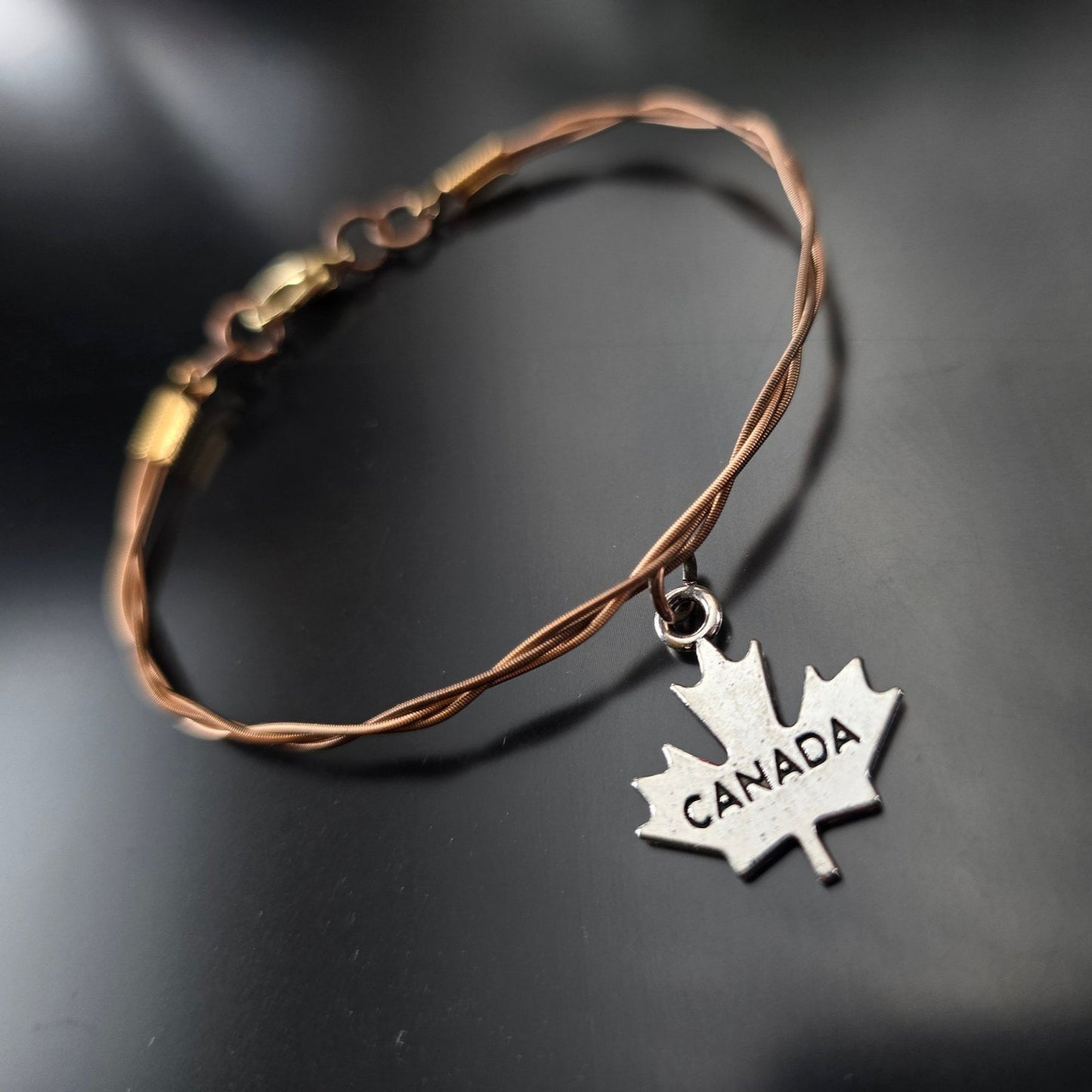bronze coloured guitar string bracelet with silver coloured canada maple leaf pendant