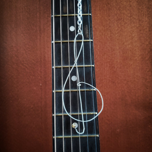 rearview mirror decoration in the shape of a treble clef, made from an upcycled guitar string - behind it is the neck of a burgundy guitar