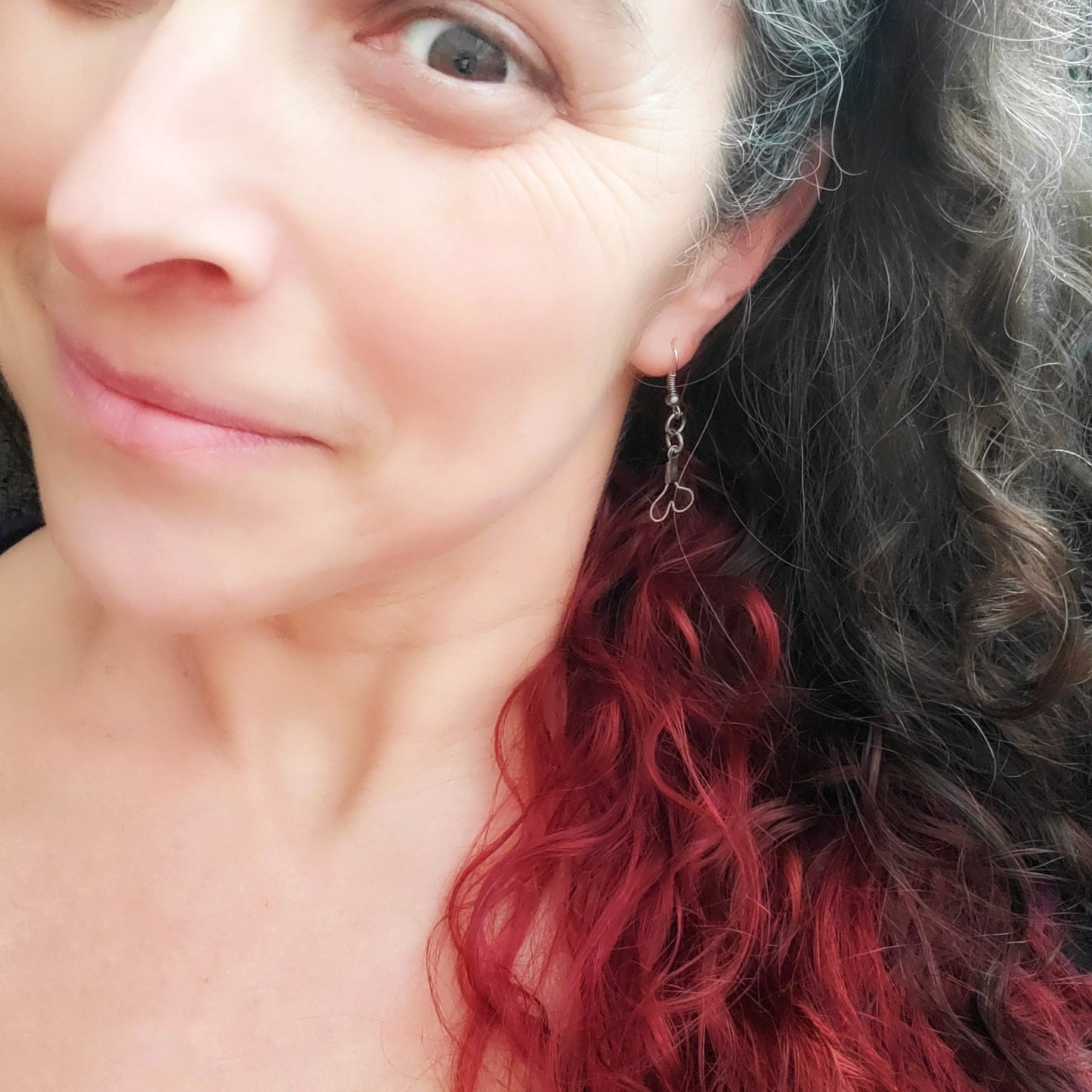 side of a woman's head with grey, brown and red hair- she is wearing a pair of earrings in the shape of upside down hearts, made from upcycled guitar strings