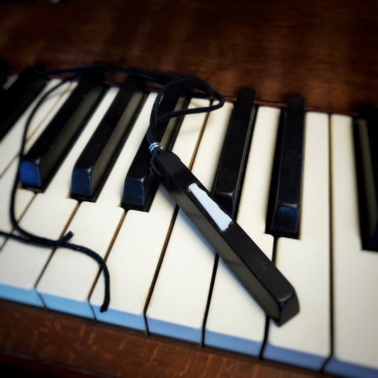 necklace made from an ebony piano key and a piece of piano key ivory with a leather lanyard sitting on a set of piano keys