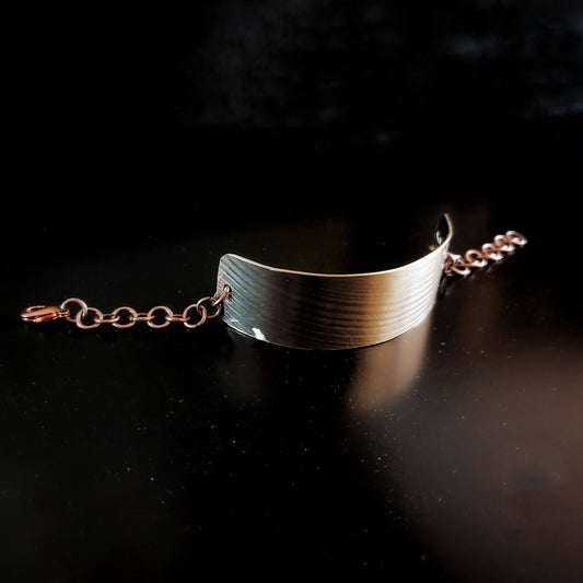 bracelet made from a rectangular piece of upcycled cymbal and copper coloured chain - black background