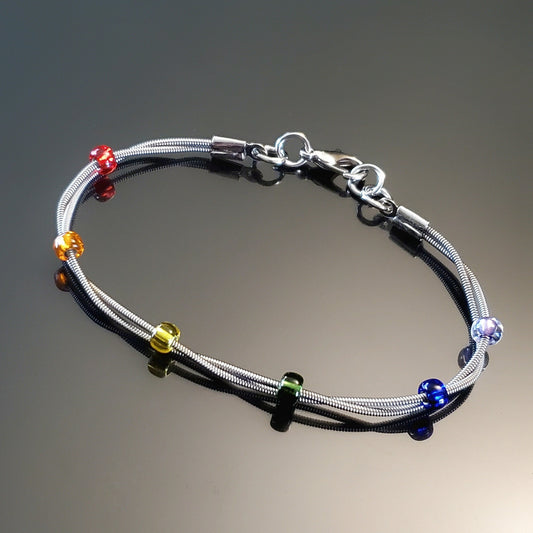 clasp style bracelet made from two upcycled guitar strings - 6 glass beads represent the colours of the LGBTQ flag (red, orange, yellow, green, blue and purple)