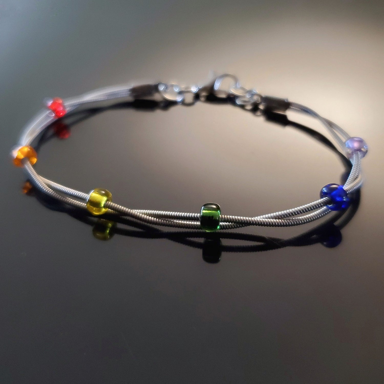 clasp style bracelet made from two upcycled guitar strings - 6 glass beads represent the colours of the LGBTQ flag (red, orange, yellow, green, blue and purple)