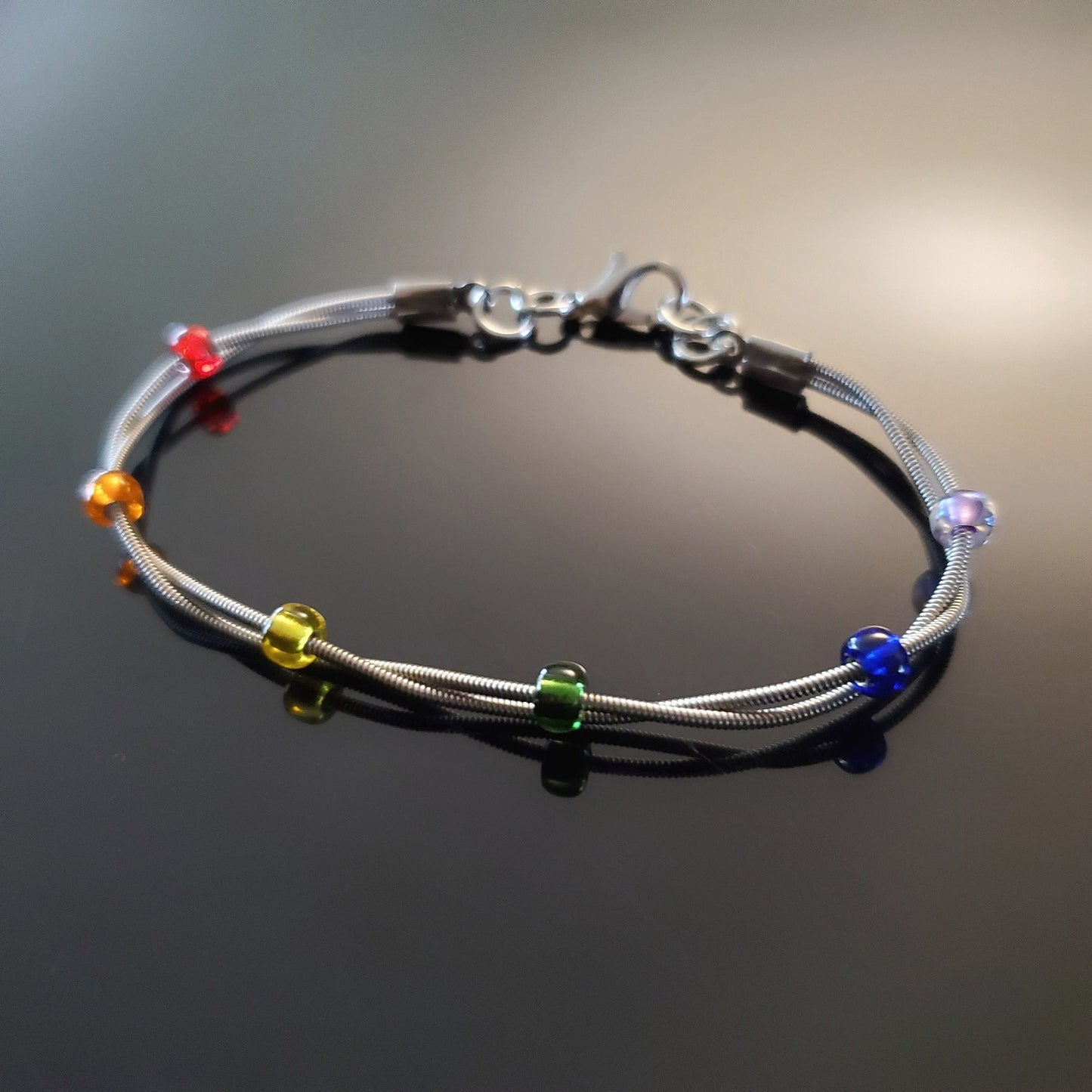clasp style bracelet made from two upcycled guitar strings - 6 glass beads represent the colours of the LGBTQ flag (red, orange, yellow, green, blue and purple)