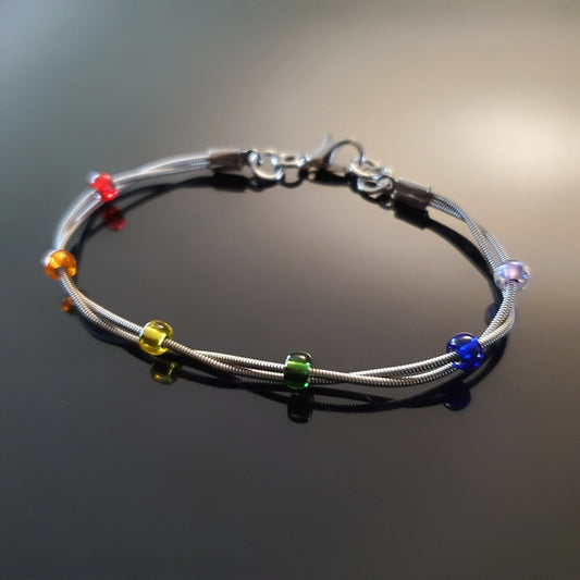 clasp style bracelet made from two upcycled guitar strings - 6 glass beads represent the colours of the LGBTQ flag (red, orange, yellow, green, blue and purple)
