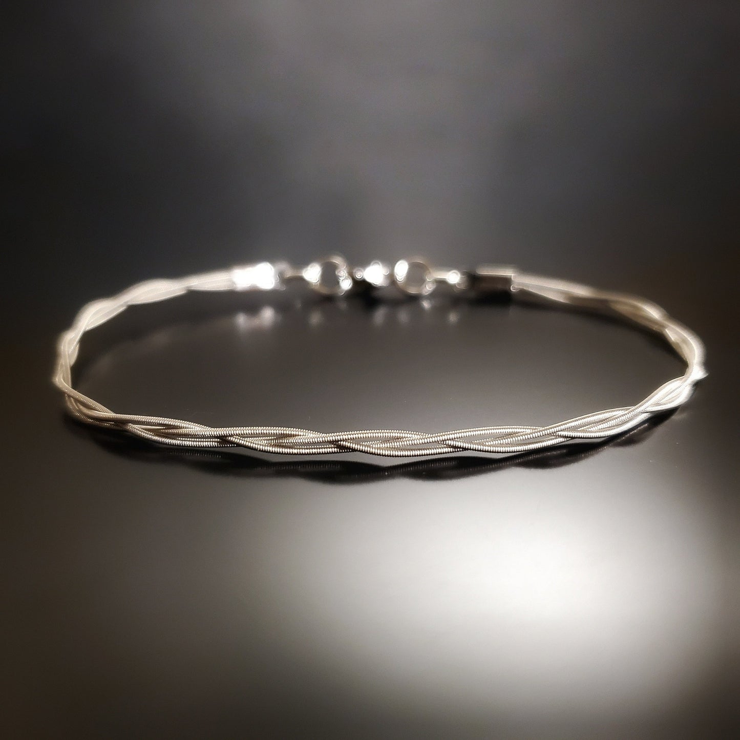 bracelet made from 3 strands of guitar strings braided together on a black background