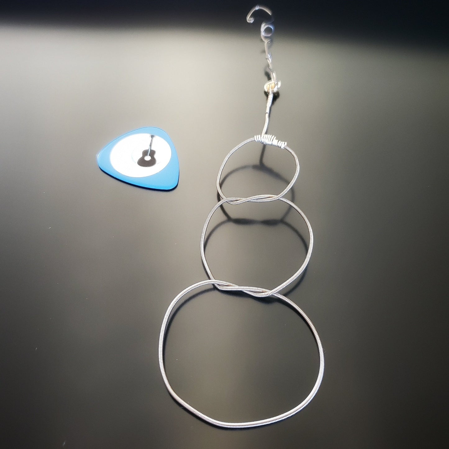 Christmas ornament in the shape of a snowman, made from an upcycled guitar string - on the left is a blue guitar pick with an image of a black guitar