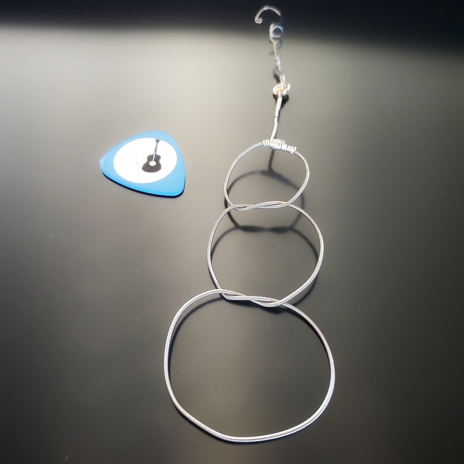 Christmas ornament in the shape of a snowman, made from an upcycled guitar string - on the left is a blue guitar pick with an image of a black guitar