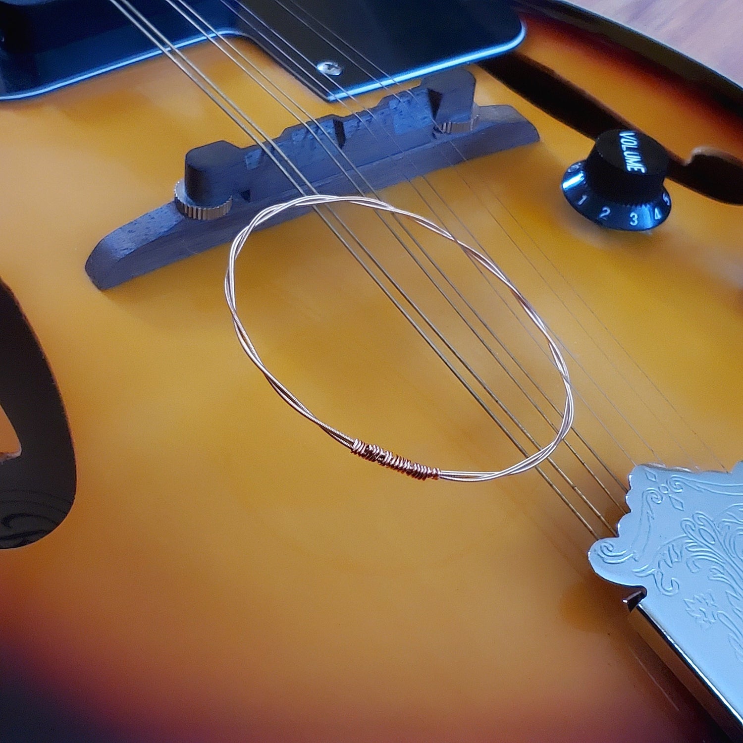 bangle style bracelet made from an upcycled mandolin string sitting on the strings of a gold coloured mandolin