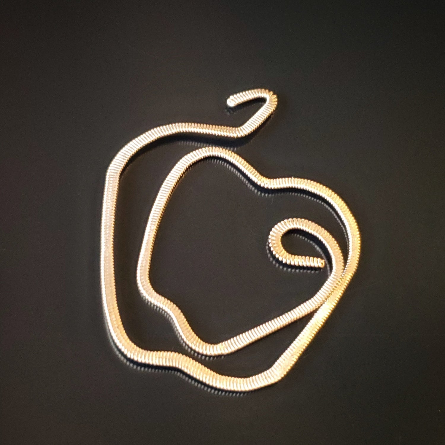 gold coloured guitar string bookmark teacher gift shaped like an apple on a black background