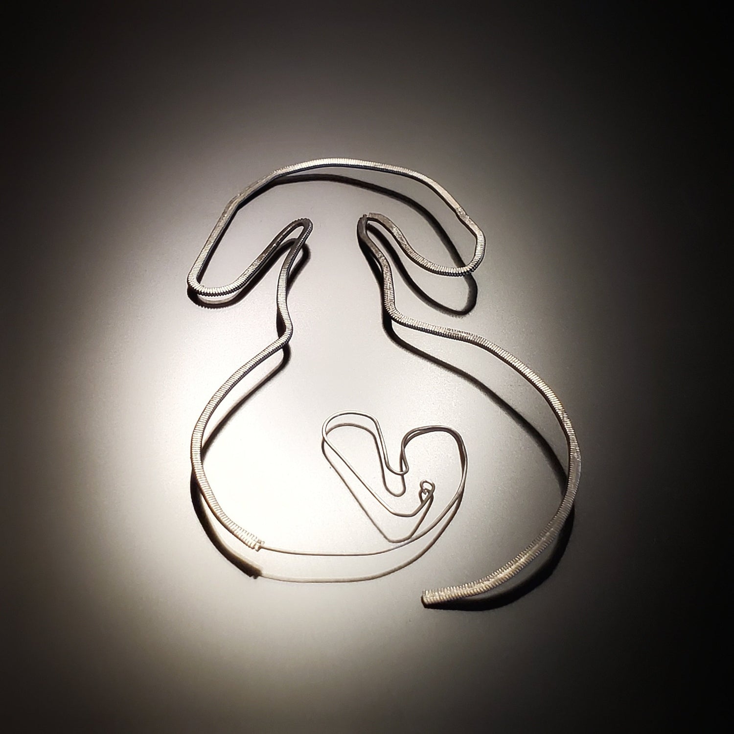 a bookmark in the shape of a dog, made from an upcycled guitar string hammered flat - black and grey background