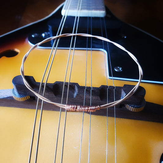 bangle style bracelet made from an upcycled mandolin string sitting on the bridge of a gold coloured mandolin