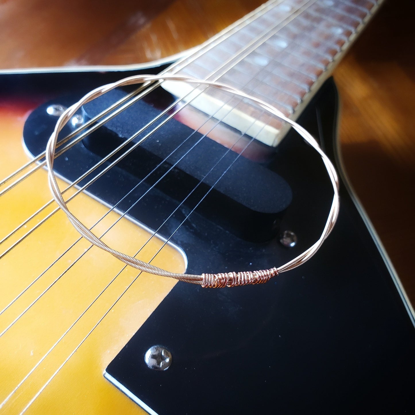 bangle style bracelet made from an upcycled mandolin string sitting on the bridge of a gold coloured mandolin