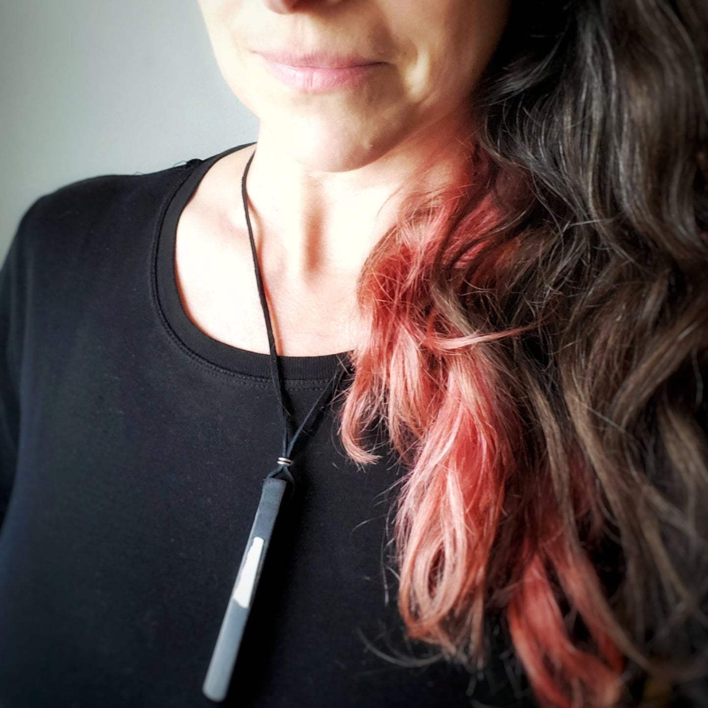 woman in glasses wearing a necklace made from an ebony piano key and a piece of piano key ivory with a leather lanyard