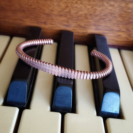 copper cuff bracelet made from upcycled piano string on piano keys