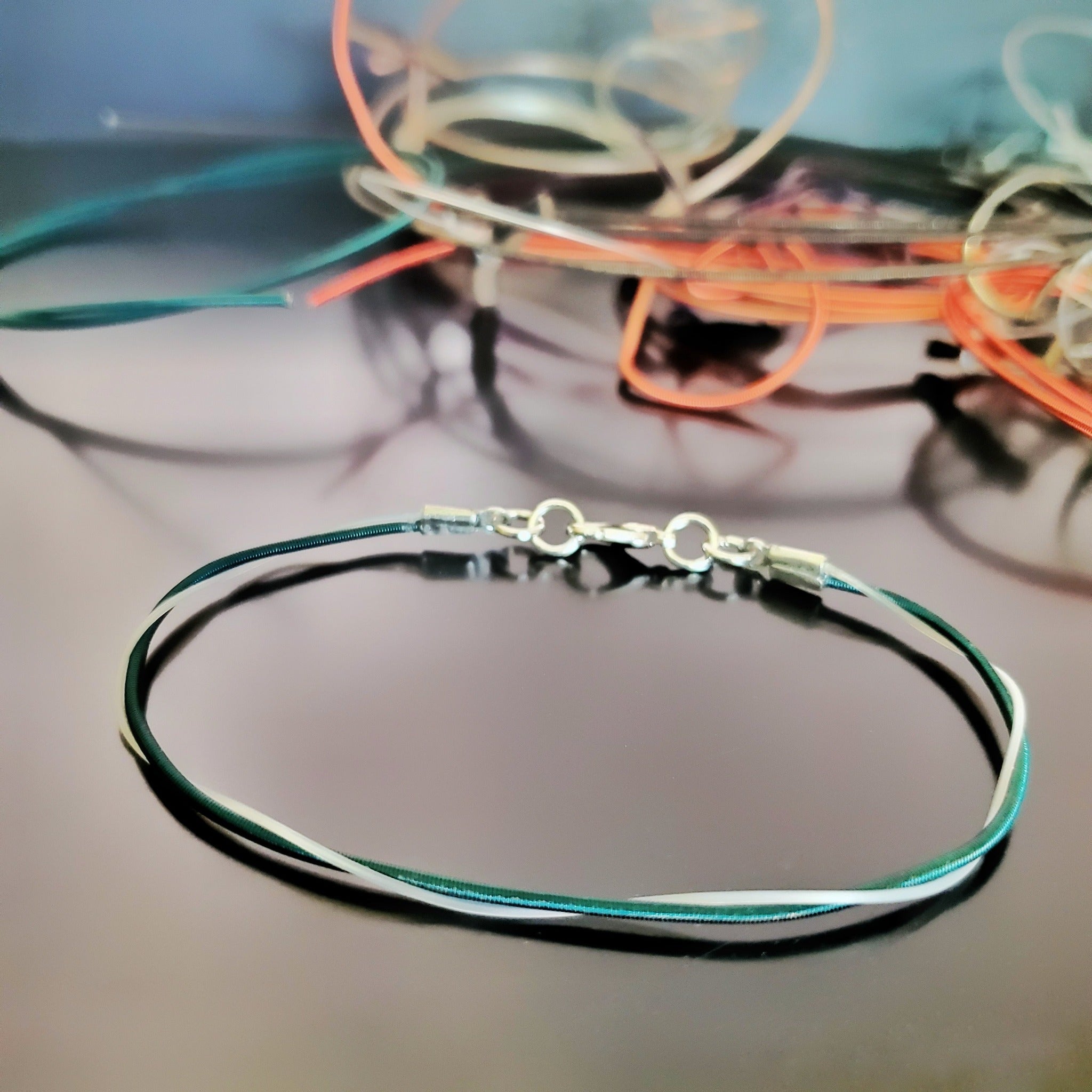 Upcycled Green harp string bracelet on a black background with various harp stings in the background