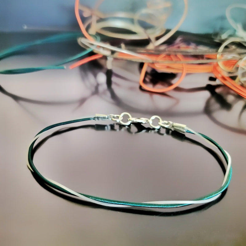 Upcycled Green harp string bracelet on a black background with various harp stings in the background