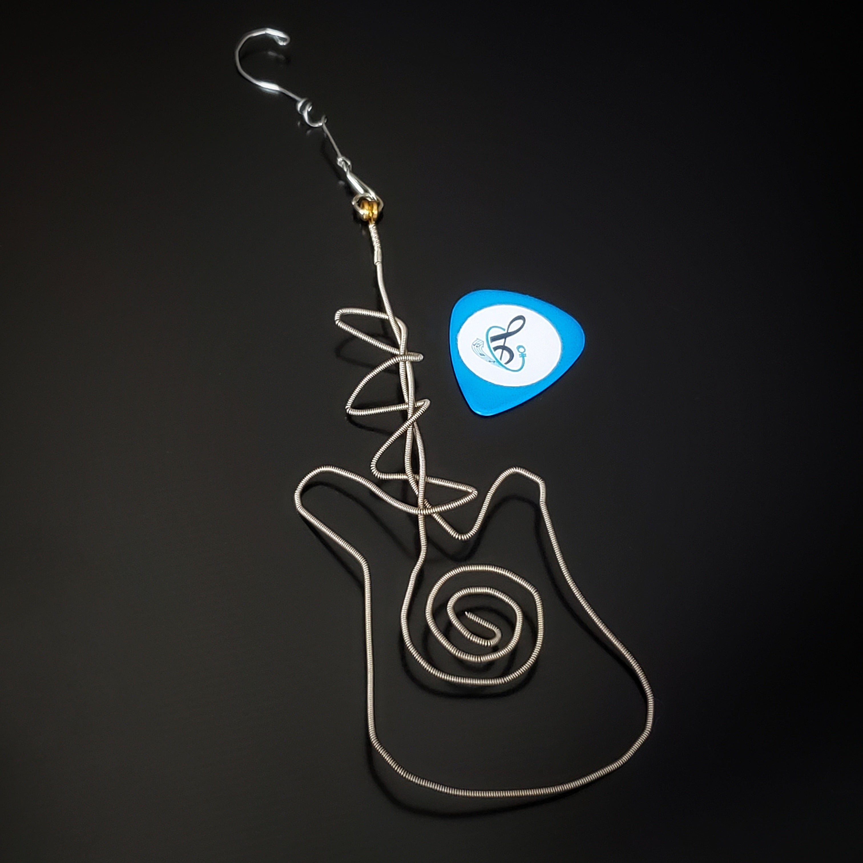 a Christmas ornament made from an upcycled guitar string in the shape of a guitar next to a blue guitar pick - black background