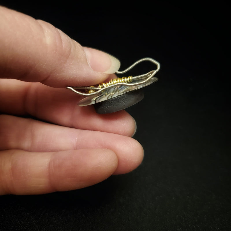 fingers holding a magnet made from an upcycled guitar string shaped like a butterfly sitting on top of a black round magnet- black background