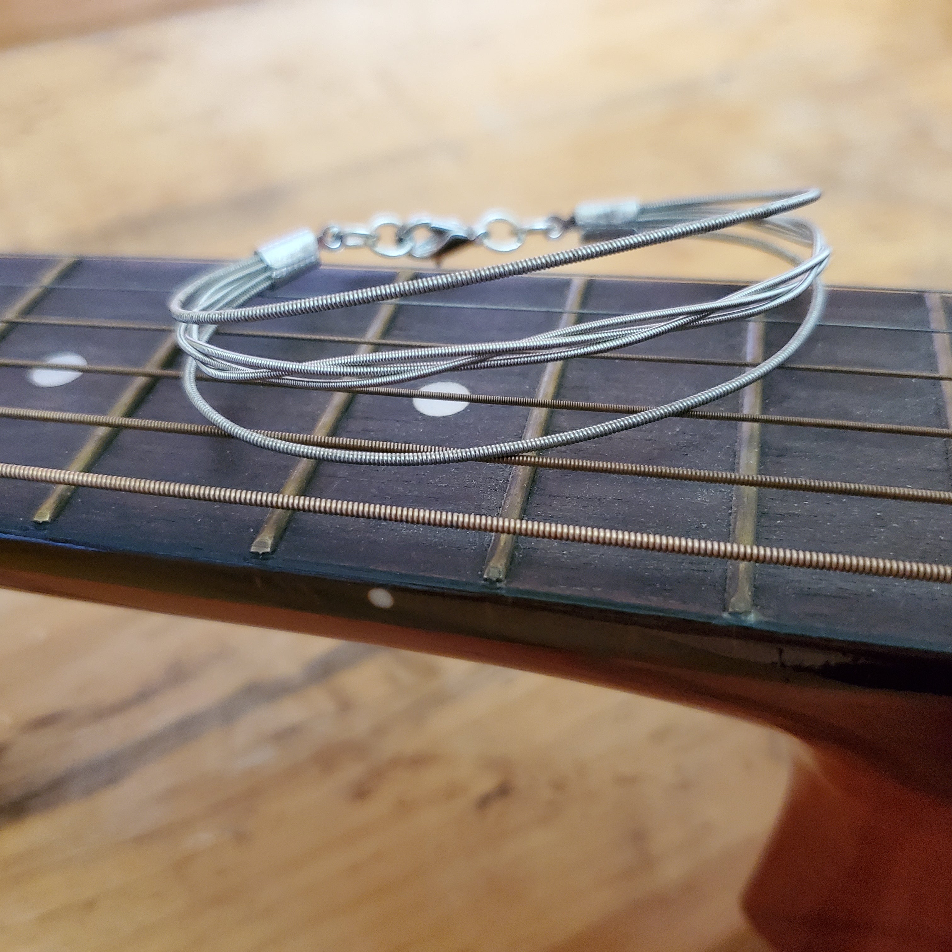 silver bracelet made from upcycled guitar strings - a braided center with a single string on each side- sitting on the bridge of a guitar